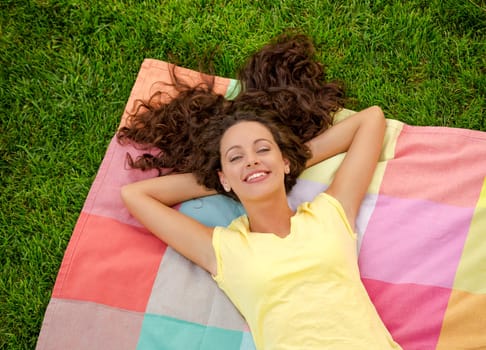 Smiling young woman lying on her back on a blanket and relaxing