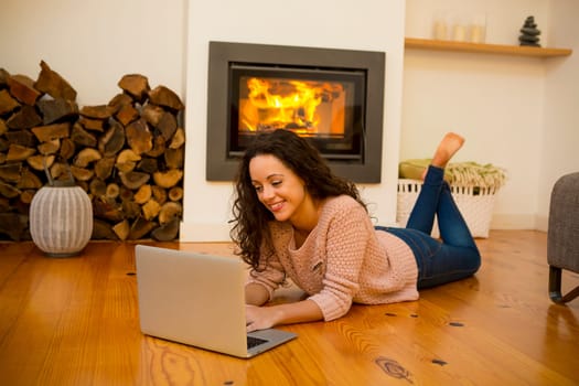 Beautiful woman working with a laptop at the warmth of the fireplace