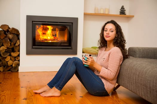 Beautiful woman drinking a hot tea at the warmth of the fireplace