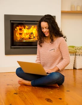 Beautiful woman working with a laptop at the warmth of the fireplace