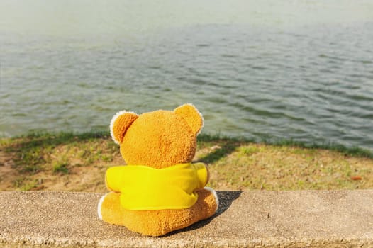 Teddy bear relax on the chair with riverside blur background
