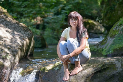Nice girl posing on a rock in the middle of a little river