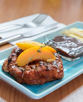Grilled pork steak fillet with Peach and French fries on blue plate and cutlery over wooden table