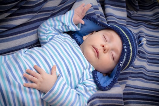 Newborn baby boy with striped hat and pajama sleeping on a blue blanket