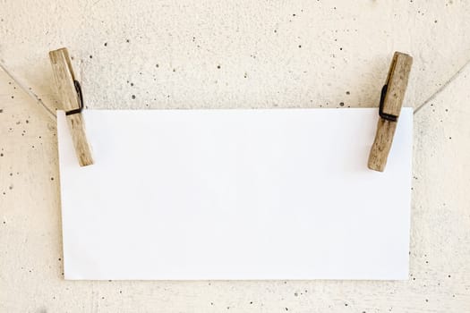 Clothespins holding on clothesline or rope holding white blank paper card on plaster background
