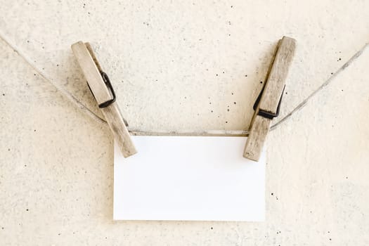 Clothespins holding on clothesline or rope holding white blank paper card on plaster background