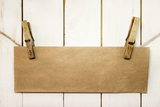 Clothespins holding on clothesline or rope holding brown blank craft paper card on wooden background
