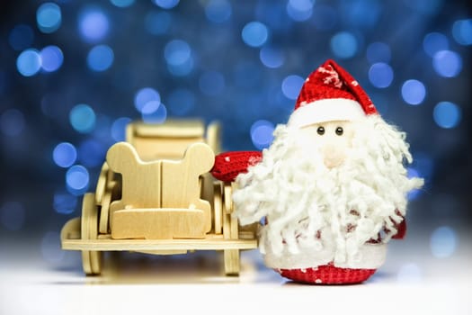Santa Claus or Father Frost with old vintage wooden automobile on christmas lights background. Main focus of image on Santa Claus and selective on face standing wood car