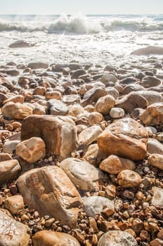 Waves crashing on a rocky beach as the tide is coming in, leaving white wake behind as the water resides.