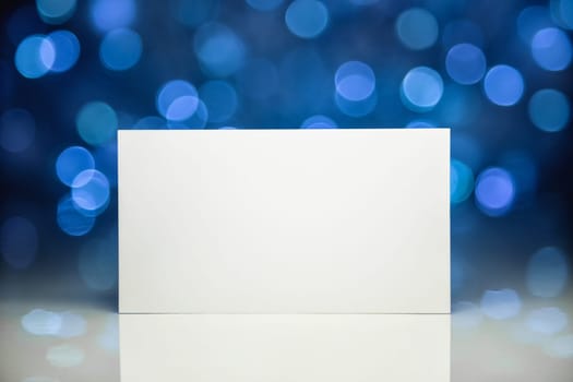 Greeting white blank card with reflection on Christmas lights background on white surface
