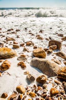 Waves crashing on a rocky beach as the tide is coming in, leaving white wake behind as the water resides.
