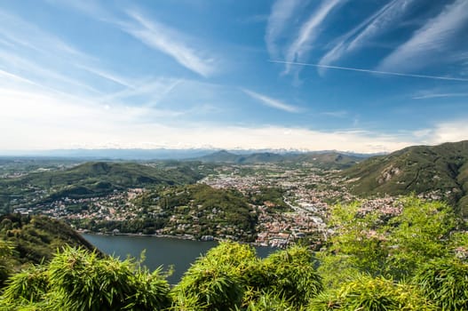 A view of Lake Como, the Town called Como and the Alps in the far distance with blue skys and white clouds.