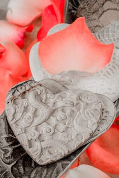 Pocelain hearts in a silver bowl together with light red rose peddles.