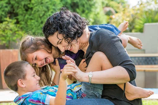 Young mother, son and daughter playing outside on the lawn in sunny weather, having fun, laughing with joy.