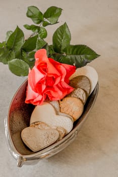 Hearts made from porcelain with the imprints of doylies placed inside a silver bowl with a red rose on top.