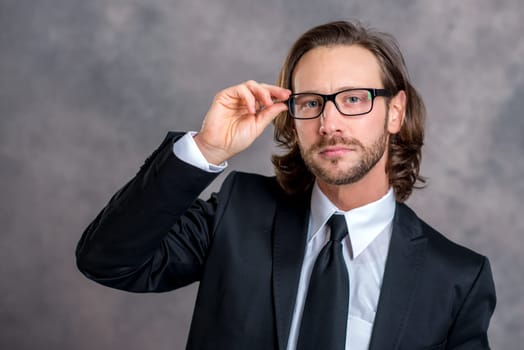 portrait of a young business man in black suit in front of gray background