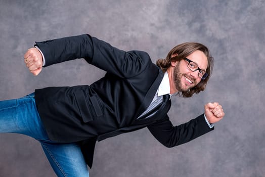 portrait of a young active business man in black suit in front of gray background
