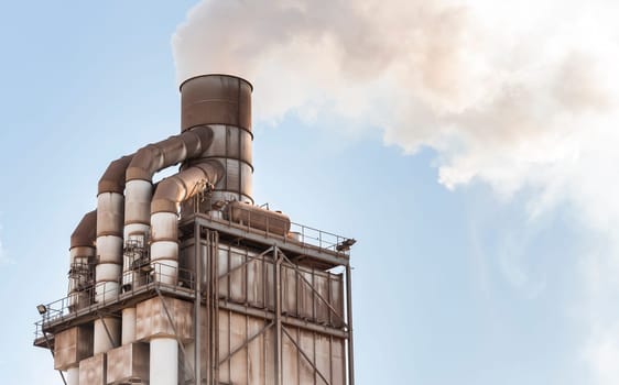 Old smokestack that emits white smoke in the clear blue sky.
