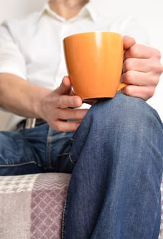 Man resting on a sofa and holding a cup of coffee