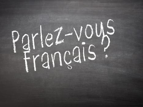Learning language - French. Learning French language concept of teacher or student writing parlez-vous francais (do you speak French) on blackboard / chalkboard.