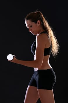 Young woman doing exercise with dumbbells, over black