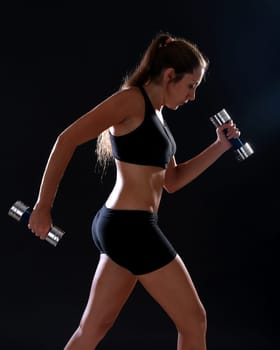 Young woman doing exercise with dumbbells, over black
