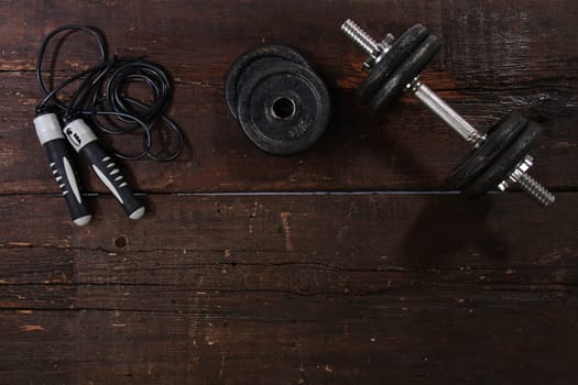 Dumbbell and a skipping rope on a rusty wooden floor