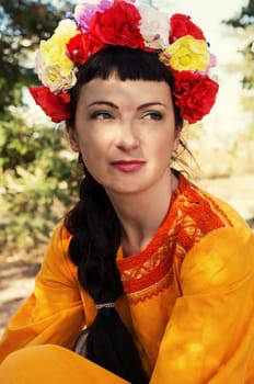 charming woman in wreath of roses on her head on the background of nature