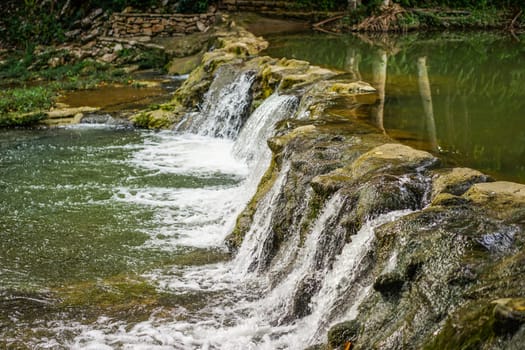 landscape with small waterfall by the lake on a summer day and green moss on the stones