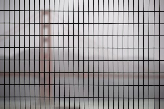 The Golden Gate bridge blurred behind a fence in this rainy weather.
