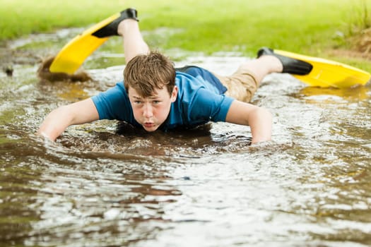 Serious male teenager in diving fins trying to swim in large shallow backyard puddle