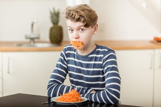 Waist Up of Boy with Wavy Blond Hair Sitting at Kitchen Table with Plate and Mouthful of Shredded Carrots and Looking Surprised - Humorous Nutrition Concept Image