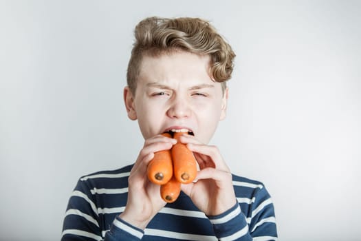 Head and Shoulders Portrait of Boy with Wavy Hair Stuffing Three Large Carrots into Mouth in front of White Studio Background with Copy Space - Health and Nutrition Humorous Image