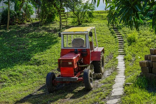 old red tractor, parked on the green grass. The brakes are uncertain, so there&#39 s been a rock at one wheel, so it does not roll down the hill