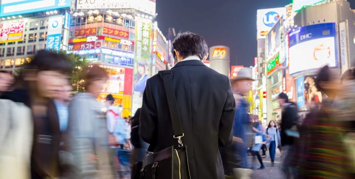Solitary japanese corporative businessman in suit, after work, waiting in crowd on Shibuya crossing, famous shopping and entertainment district of Tokyo, Japan.