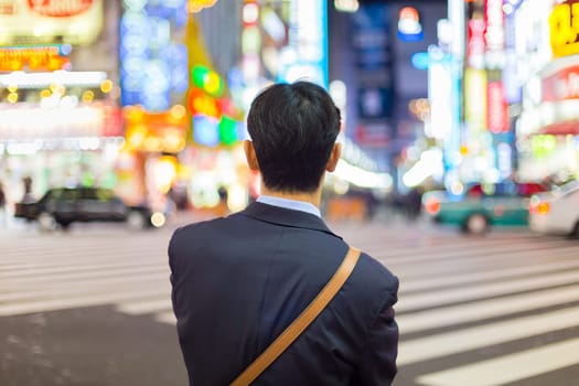 Solitary japanese corporative businessman in suit, after work, waiting on crossroad in Kabukicho, entertainment and red-light district in Shinjuku, Tokyo, Japan.