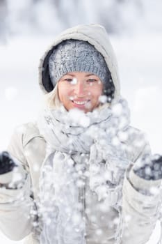 Cute casual young woman playing with snow in winter time.