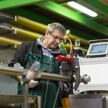 Industrial operator setting  computer controlled process of orbital welding machine in inox pipes manufacturing workshop.