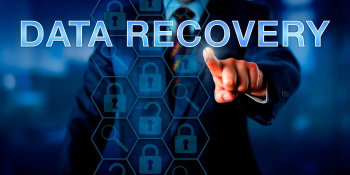 Manager is pointing at DATA RECOVERY on a touch screen. Business metaphor and technology concept. Magnifier glass icons do reference analyzing tools and locked padlocks represent encrypted files.