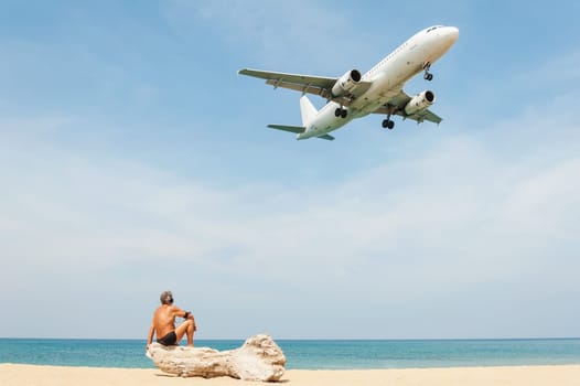 Wood table top on blurred blue sea and white sand beach with some people and plane