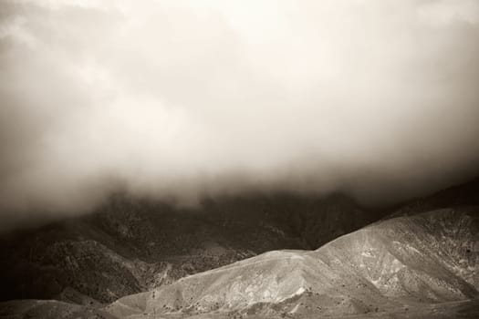 A cloud and fog pushes over the mountain ridges to the ground.