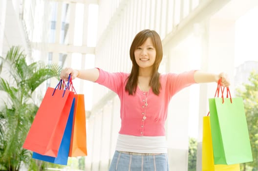 Happy young Asian woman with shopping bags walking out the mall. Beautiful golden sunlight at background.