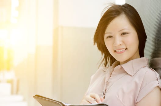 Young Asian woman executive smiling and standing at an office environment, natural golden sunlight at background.