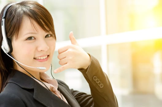 Portrait of a young Asian customer support with headset smiling, at an office environment, natural golden sunlight at background.