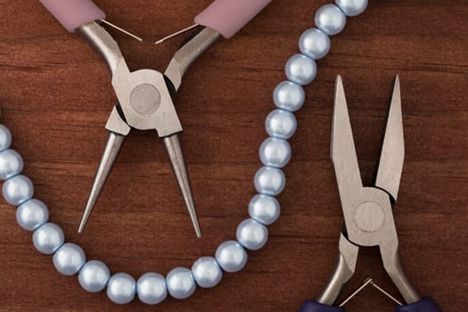 Two types of jewelry making pliers and a string of blue pearls for jewelry making.