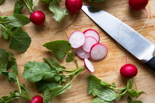 Radish slices and whole radishes with knife on cutting board.