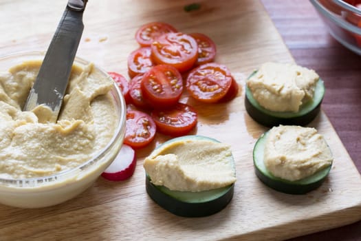 Making healthy snacks with cucumbers, hummus, tomatoes and radishes.