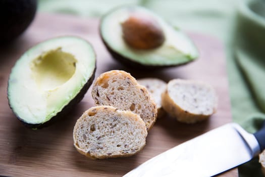 Fresh avocado cut in half and small slices of bread for making avocado toast.