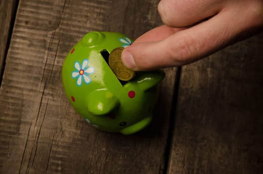 Male hand with a coin and a piggy bank on wood, saving money concept