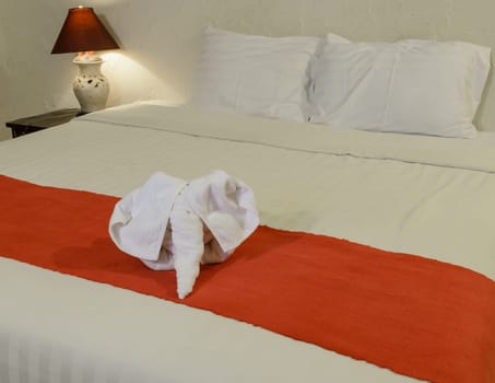 White towel in elephant shape on white bed in Thai style hotel bedroom